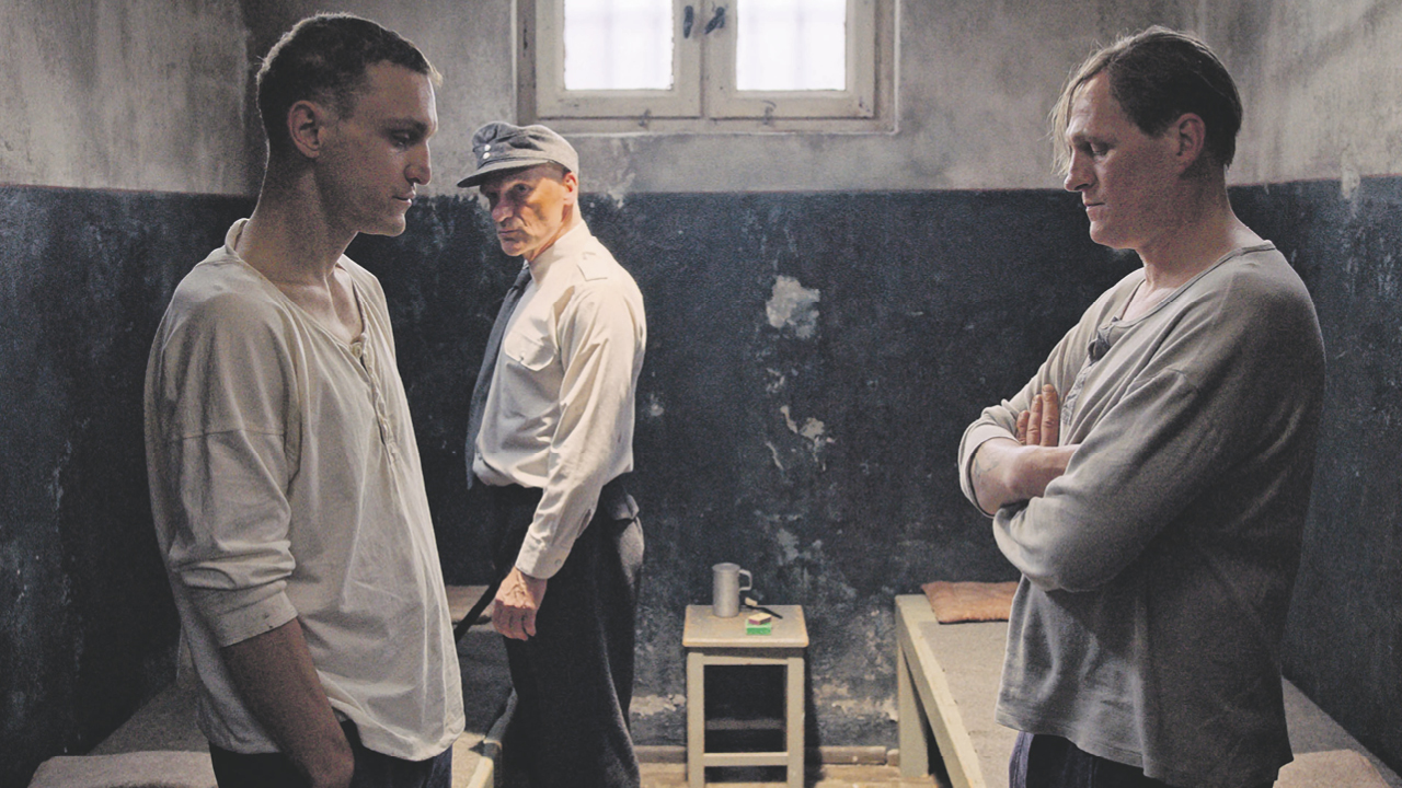 Szene eines Films aus dem Gefängnis - zwei Männer stehen sich gegenüber, hinter ihnen ein Wärter mit Mütze