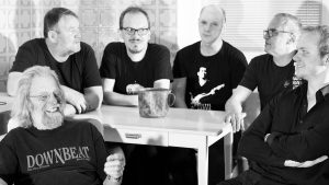 Schwarz-weiß Bandfoto mit sechs Männern, an einem Tisch sitzend